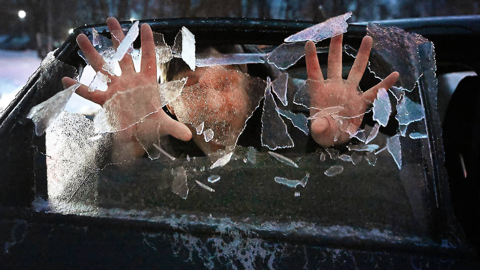 Мужчина разбивает наледь на боковом окне автомобиля, образовавшуюся после «ледяного дождя»