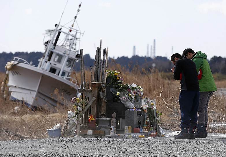 Молитва за жертв землетрясения и цунами в городе Нами. 11 марта Япония отмечает третью годовщину удара стихии, унесшего жизни тысяч людей и спровоцировавшего крупную аварию на АЭС «Фукусима» (на заднем плане)