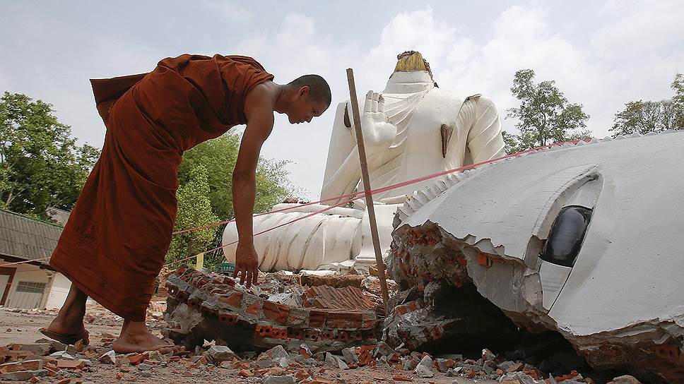 Буддийский монах посматривает статую Будды, поврежденную в результате землетрясения в городе Чианграй, Таиланд