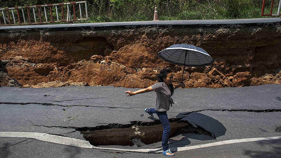 Женщина перепгыривает через яму на шоссе, поврежденном в результате землетрясения в городе Чианграй, Таиланд