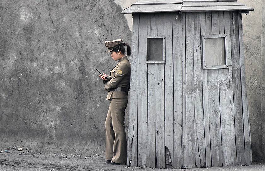 Северокорейская женщина-солдат с мобильным телефоном возле поста часового на берегу реки Ялуцзян, разделяющей КНДР и Китай