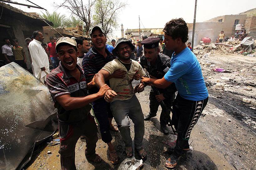 Люди на месте взрыва автомобиля, начиненного взрывчаткой в иракском городе Эль-Искандария