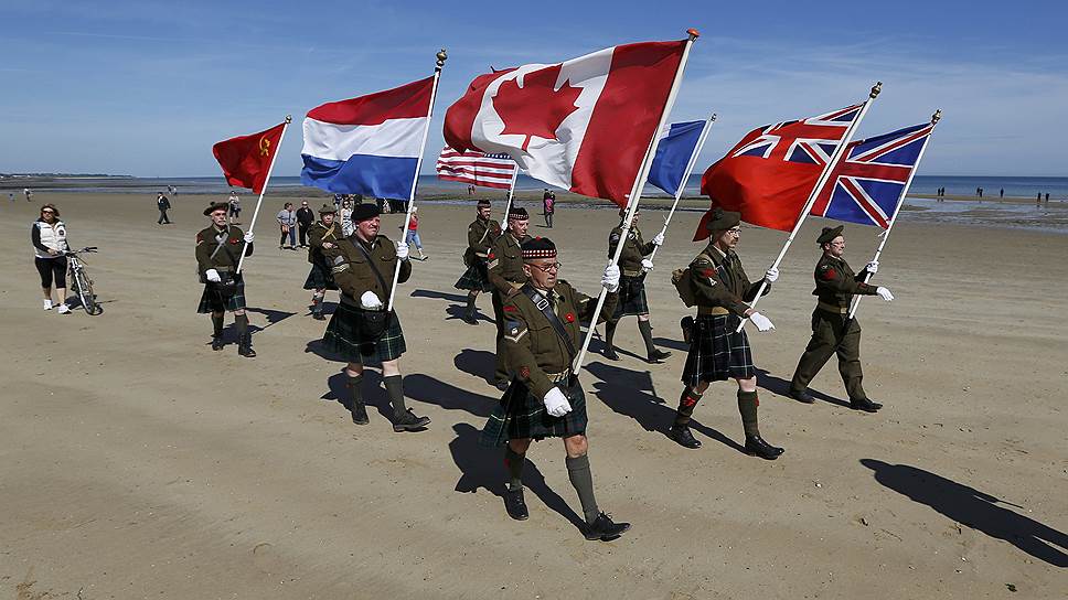 Голландские любители истории маршируют с флагами стран-союзников в зоне высадки канадских войск на пляже Джуно