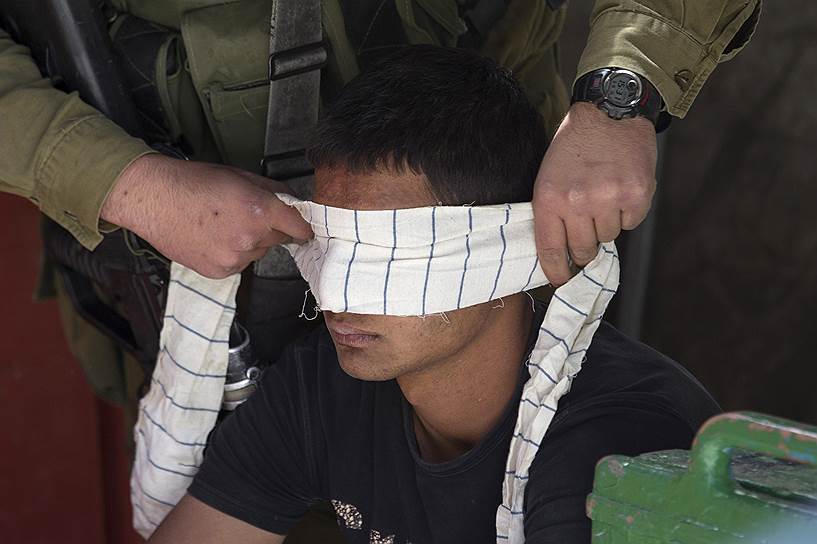 Израильский военный завязывает глаза палестинцу, задержанному во время столкновений в Хеброне