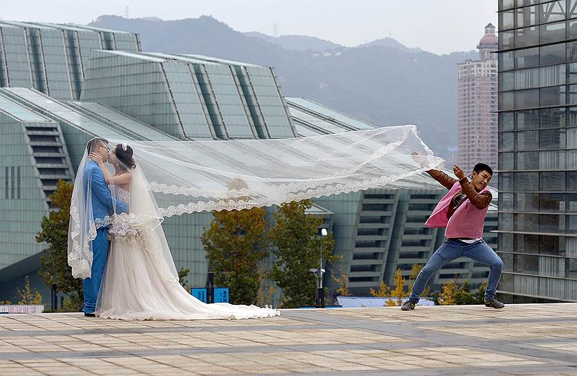 Гонконг, Китай. Ассистент поддерживает фату невесты во время свадебной фотосессии
