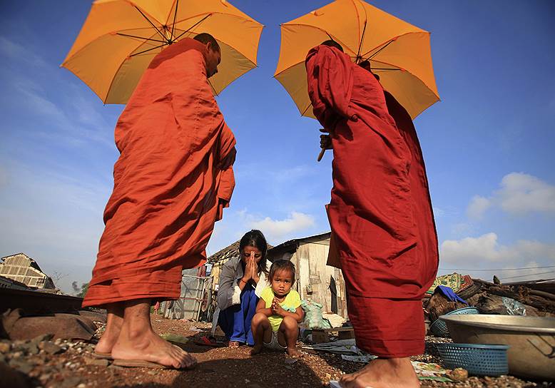 Пном Пень, Камбоджа. Женщина с ребенком молятся после подаяния монахам милостыни