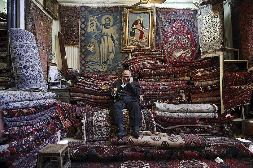 Тегеран, Иран. Мужчина разговаривает по сотовому телефону в своем магазине ковров на старом базаре