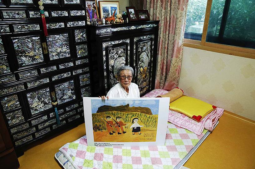 Жертва сексуального рабства 89-летняя Ким Бок Дон из Южной Кореи держит в руках одну из своих картин в приюте для бывших секс-рабынь. Согласно показаниям Ким, в возрасте 14 лет ее привезли на одну из «станций утешения», где принуждали обслуживать около 30 мужчин в сутки
