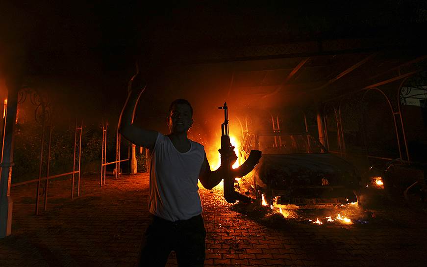 11 сентября 2012 года в результате нападения на посольство США в Бенгази был убит американский посол Кристофер Стивенс. Ответственность за атаку взяла на себя запрещенная террористическая группировка «Аль-Каида» (признана террористической и запрещена в РФ). Незадолго до нападения был выпущен фильм «Невинность мусульман», вызвавший массовые протесты мусульманского населения. Кроме того, лидер «Аль-Каиды» (признана террористической и запрещена в РФ) призывал к мести за убийство главы ячейки в Ливии&lt;br>На фото: вооруженный человек на фоне горящего посольства США в Бенгази