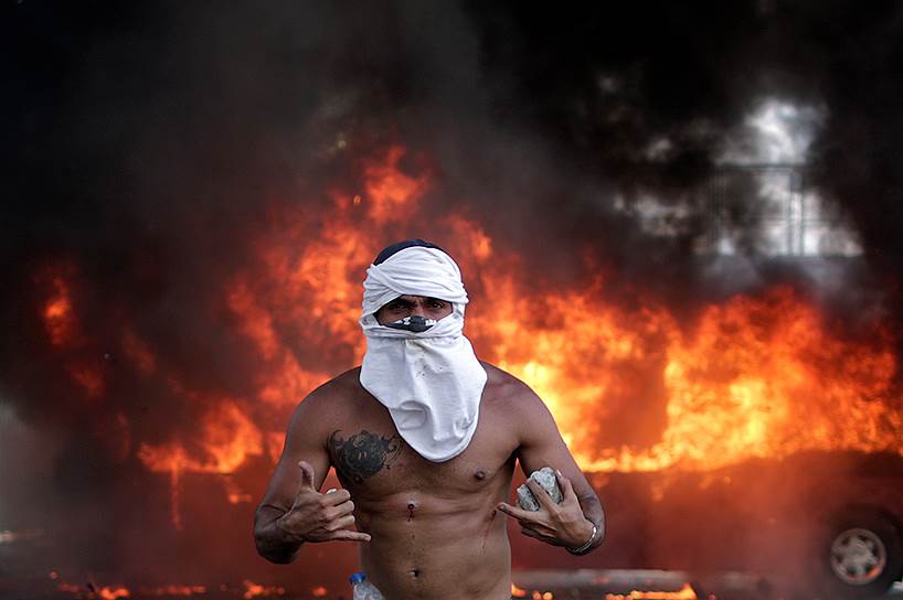 Протестующий против режима Николаса Мадуро на фоне горящего автобуса около авиабазы Ла Карлота в Каракасе