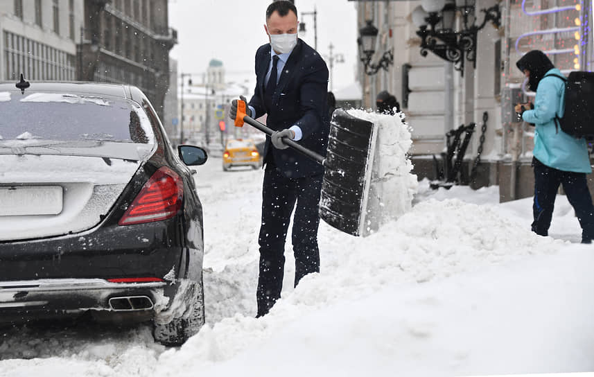 Москва. Мужчина в деловом костюме убирает снег с дороги