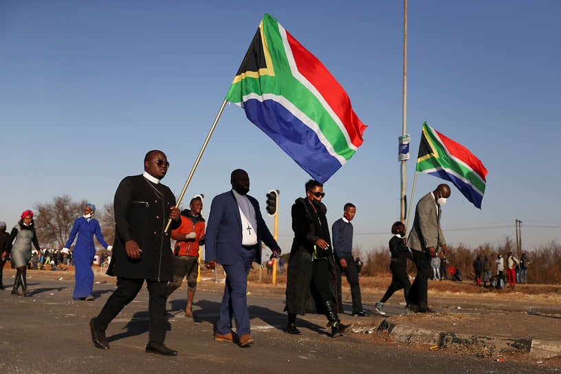 Религиозные лидеры с флагами ЮАР проходят возле разграбленного торгового центра
