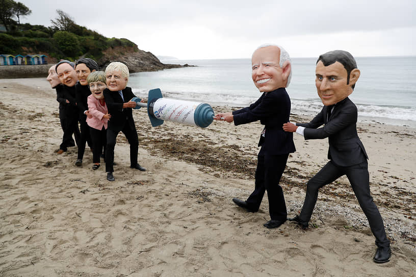 Активисты международного объединения Оксфам в масках президента США Джо Байдена, президента Франции Эмманюэля Макрона на протестной акции на пляже в Фалмуте (Британия) во время проведения саммита G7