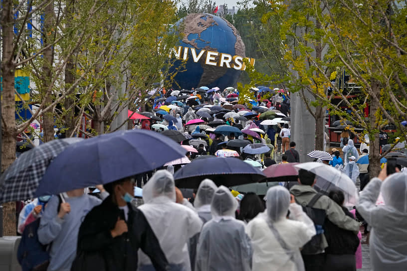Пекин, Китай. Люди в дождевиках и с зонтами перед открытием тематического парка Universal Studios Beijing