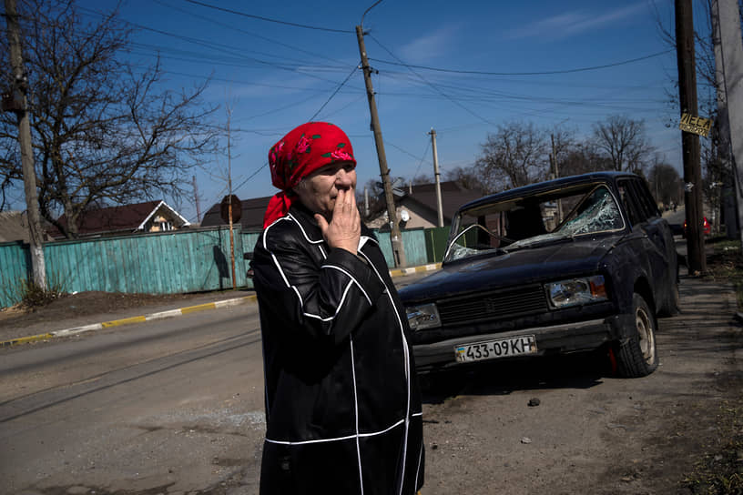 Женщина стоит рядом с разбитой машиной в Буче, пригороде Киева