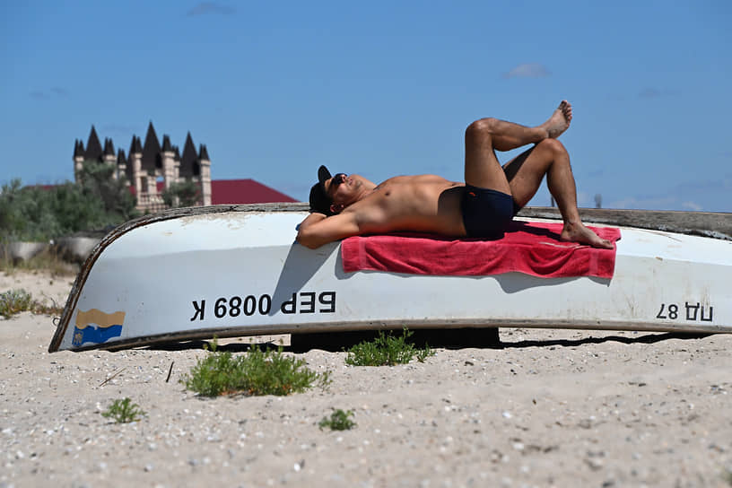 Бердянск, Запорожье. Мужчина загорает на пляже на перевернутой лодке