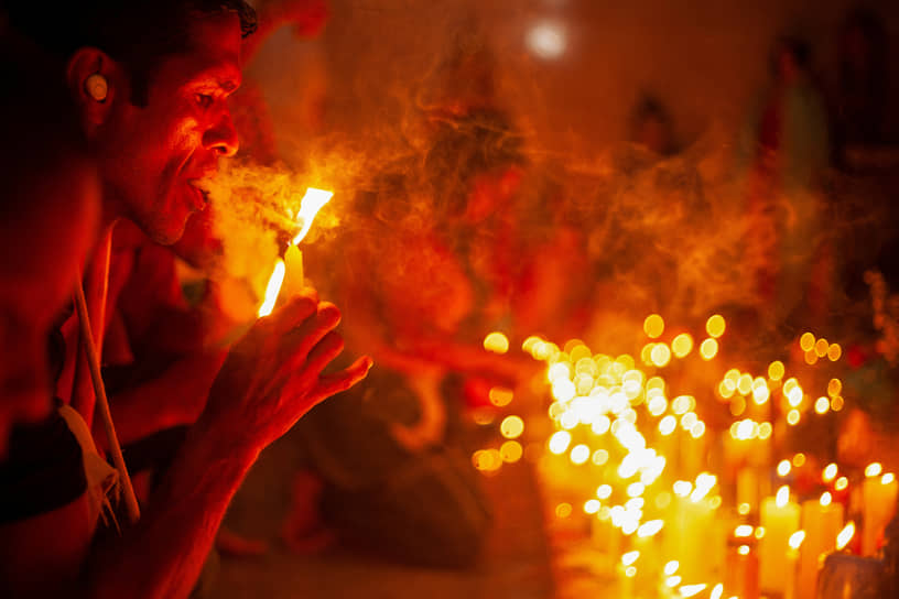 Последователь культа Марии Лионса закуривает сигару от священного алтаря