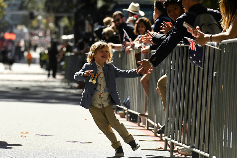 Сидней, Австралия. Ребенок, участвующий в марше в честь Дня АНЗАК, дает пять толпе