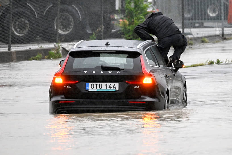 Арлов, Швеция. Мужчина выбирается из автомобиля, который застрял на затопленной кольцевой развязке