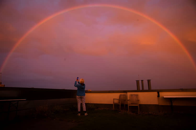 Берлин. Женщина фотографирует радугу на закате