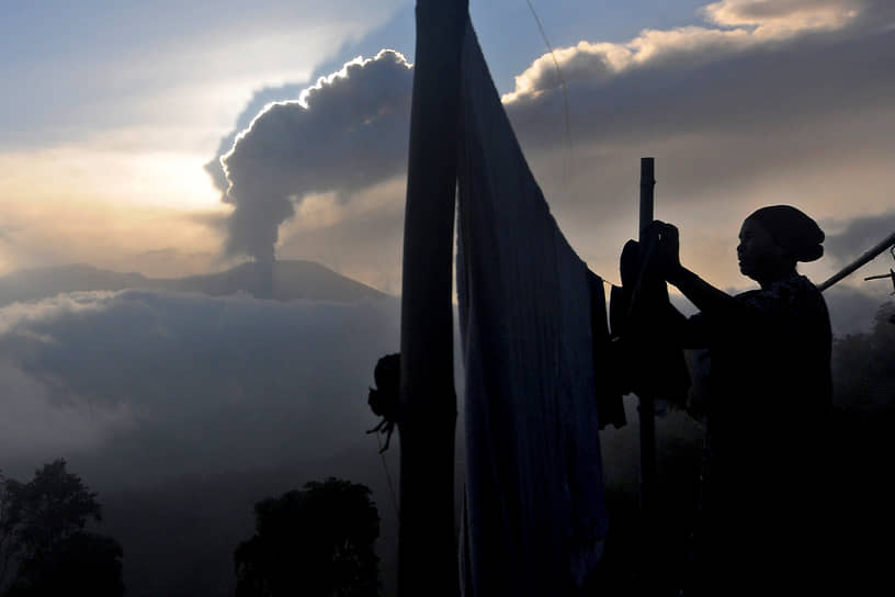 Агам, Индонезия. Женщина развешивает белье на фоне извержения вулкана Марапи