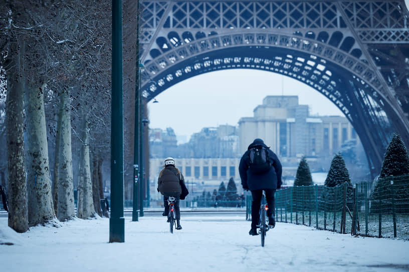 Люди едут на велосипедах по заснеженной дороге возле Эйфелевой башни в Париже, Франция