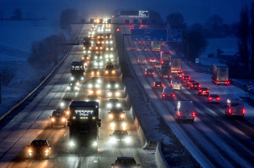 Легковые и грузовые автомобили едут по заснеженному шоссе после снегопада во Франкфурте, Германия