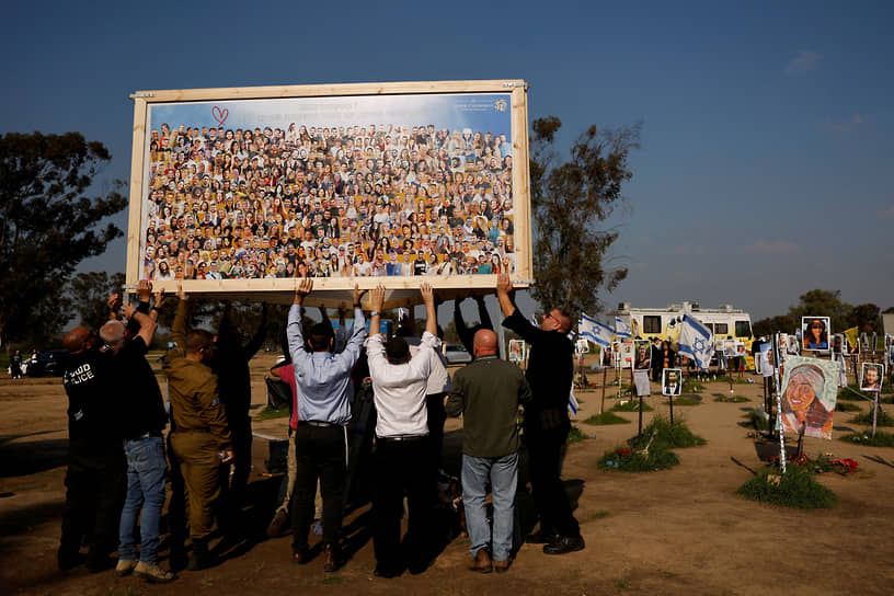 Реим, Израиль. Люди помогают поднять коллаж художника Амира Ходорова с лицами участников музыкального фестиваля «Нова», которые погибли от рук палестинских боевиков