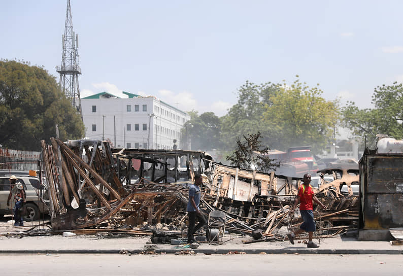 Прохожие идут мимо сожженных автобусов и автомобилей возле президентского дворца в Порт-о-Пренсе