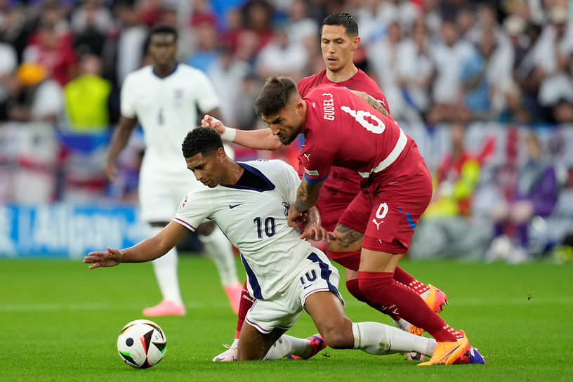 Игрок сборной Сербии Неманья Гудель (справа) пытается остановить английского футболиста Джуда Беллингема (в центре), за что получает желтую карточку