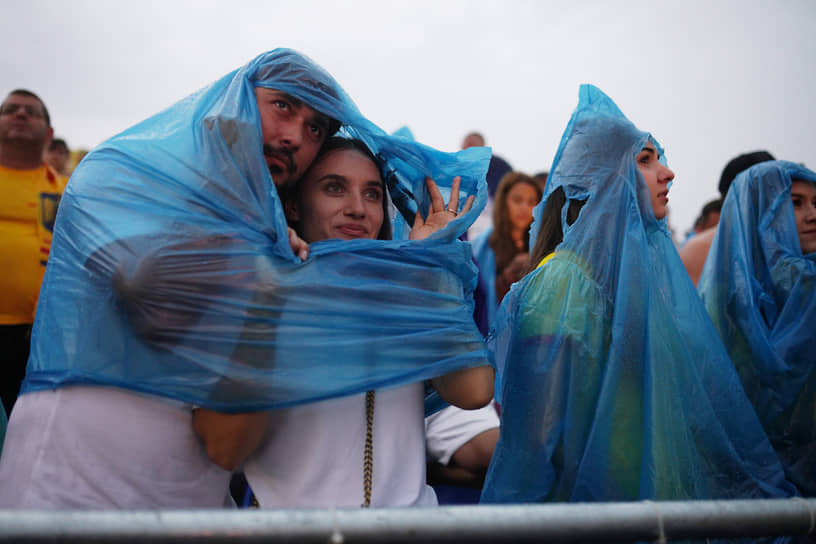 Люди укрываются от дождя во время просмотра матча Нидерланды—Румыния в Бухаресте 