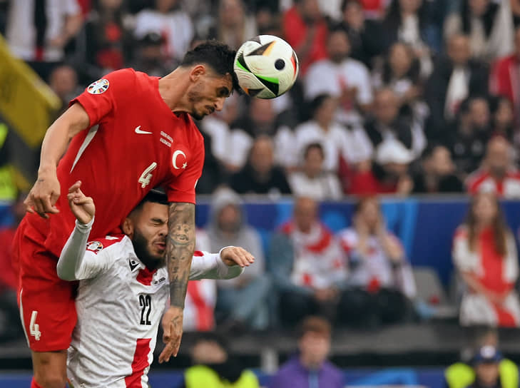 Защитник турецкой сборной Самет Акайдын принимает мяч над грузинским нападающим Жоржем Микаутадзе (справа)