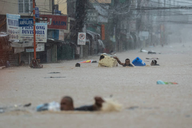 Марикина, Филиппины. Люди пробираются по затопленной дороге после сильных дождей, вызванных тайфуном «Гаеми»