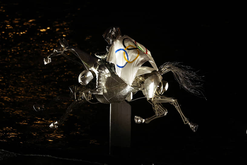 Всадница в образе Жанны д’Арк на металлическом коне едет по маршруту парада с олимпийским флагом