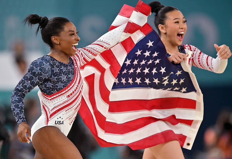 Американские гимнастки Симона Байлз (слева) и Суниса Ли держат флаг США  
