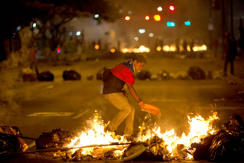 Протестующий с венесуэльским флагом на плечах на горящих баррикадах в пригороде Каракаса в 2014 году