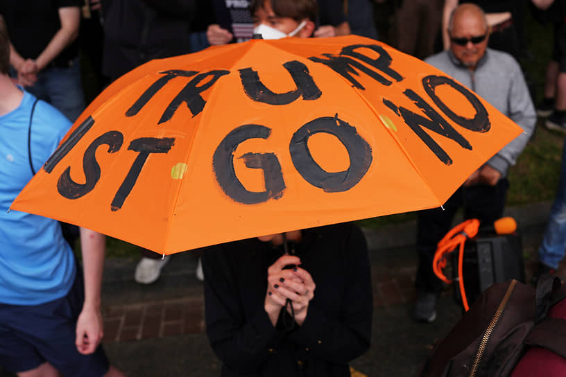 Протестующий под зонтом с надписью «Трамп должен уйти сейчас»