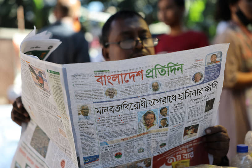 Мужчина читает газету со статьей о вынесении смертного приговора Шейх Хасине