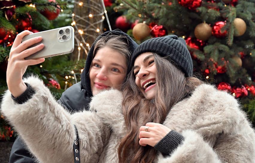 Девушки фотографируются на фоне новогодней елки