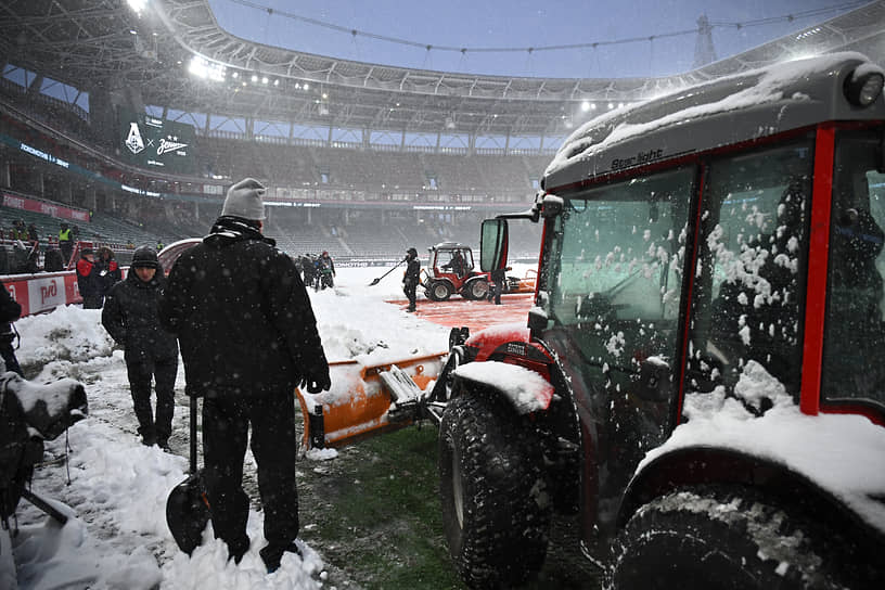 Сотрудники технической службы стадиона во время уборки снега на футбольном поле перед началом матча