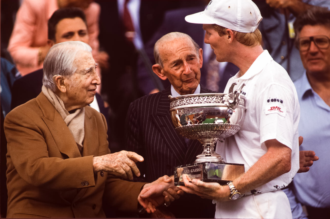 Рене Лакост умер в 1996 году в возрасте 92 лет. &lt;br> На фото: тенесист Джим Курье получает награду из рук Рене Лакоста и Анри Коше во время международных соревнований по теннису во Франции на стадионе Ролан Гаррос, 1992 года