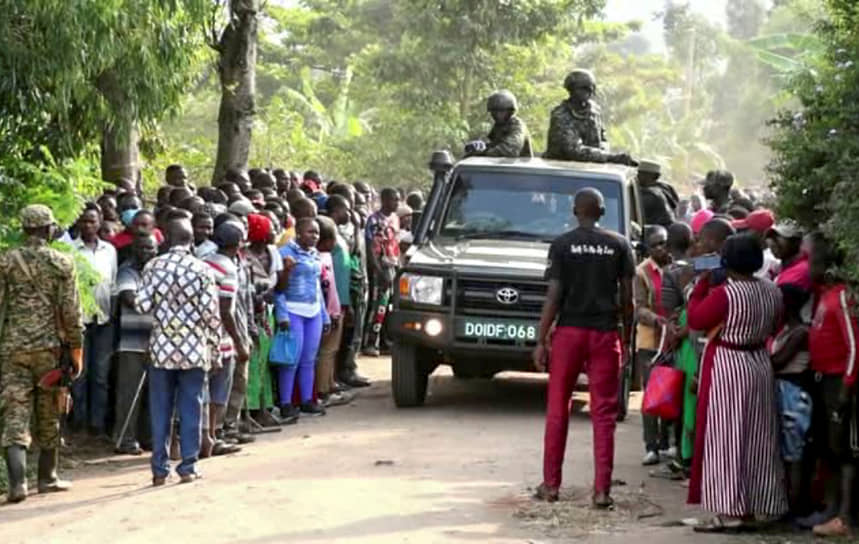 Силы безопасности проезжают мимо толпы людей, собравшихся возле средней школы после нападения, Мпондве, Уганда