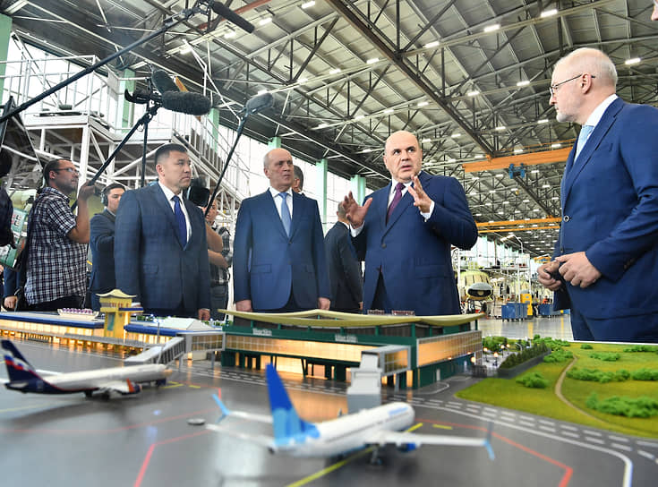 Премьер Михаил Мишустин (второй справа) рассматривает макет терминала во время посещения авиационного завода в Улан-Удэ 25 июля 2023 года