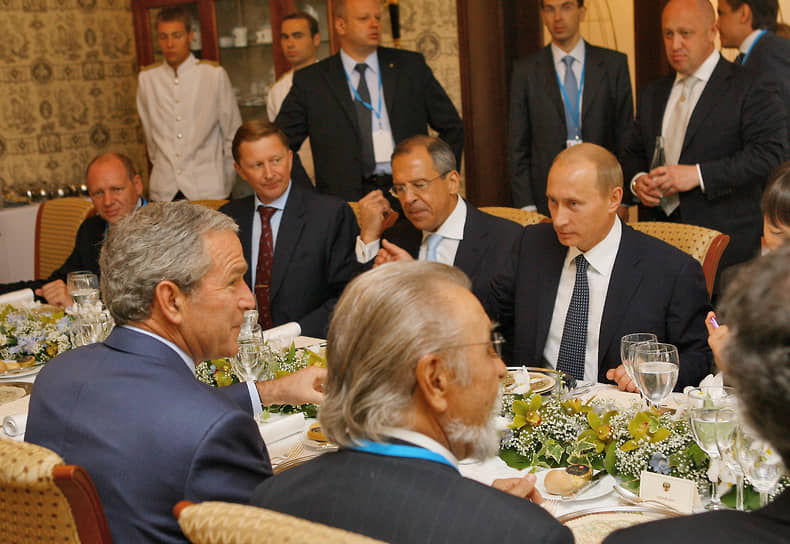 Джордж Буш (сидит спиной), Владимир Путин (напротив него), Евгений Пригожин стоит за Владимиром Путиным. Саммит G8, Санкт-Петербург, 2006 год