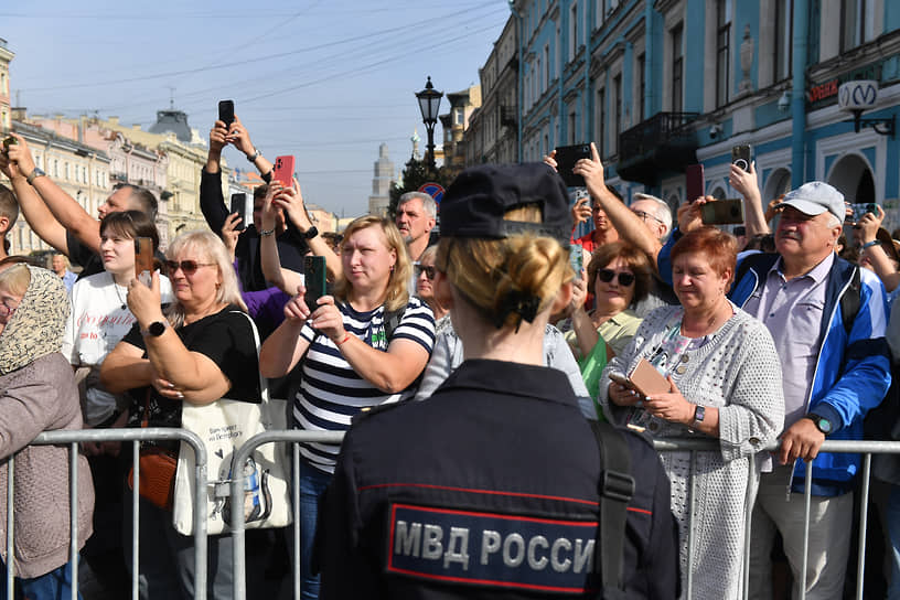 Прохожие из-за ограждения фотографируют процессию