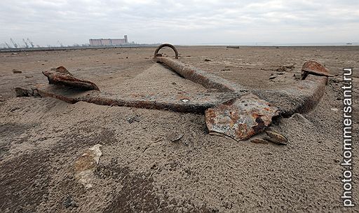 Вид обмелевшей реки Волга около Казани. Затопленный старый якорь на дне Волги. Вдалеке виден грузовой причал и элеватор речного порта.