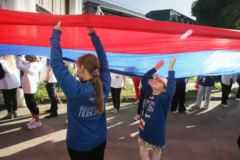Девочки-волонтеры держат флаг России, приготовленный к шествию