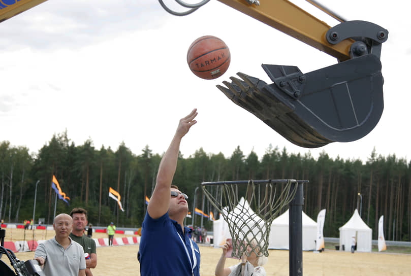 Волонтер забрасывает в ковш мини-экскаватора мяч для игры в баскетбол