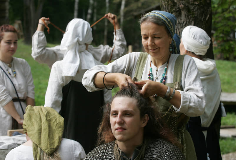 Женщина заплетает волосы участнику фестиваля в кольчуге