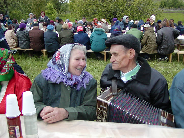 Пенсионер играет на гармони своей знакомой во время деревенского застолья
